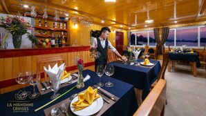 A restaurant with wooden interiors, tables set with wine glasses, plates, and cutlery. - La Mignonne Cruises (Tuan Chau)