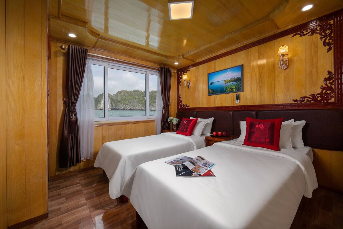 A hotel room with two beds, wooden paneling, a large window with curtains, and a painting on the wall.