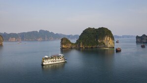 A boat on calm water with a large island in the background. - La Mignonne Cruises (Tuan Chau)