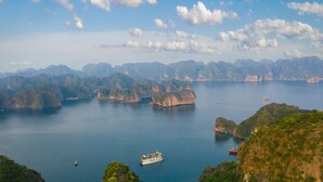 A coastal landscape with a boat docked near the shore, surrounded by lush green hills and a calm sea. - La Mignonne Cruises (Tuan Chau)