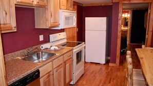 A compact kitchen with wooden cabinets, a microwave, a refrigerator, a dishwasher, and a granite countertop.