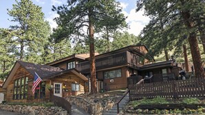 A two-story log cabin with a stone foundation, a wooden deck, and a stone wall with a wooden fence.