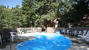 A swimming pool with a diving board, surrounded by white plastic chairs and a stone wall.