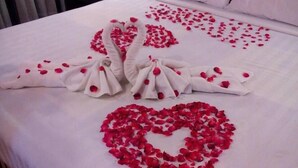 A bed with white linens, a heart-shaped arrangement of rose petals, and two swan-shaped arrangements made from towels and rose petals. - Tangerine Ville Hotel (Fang)