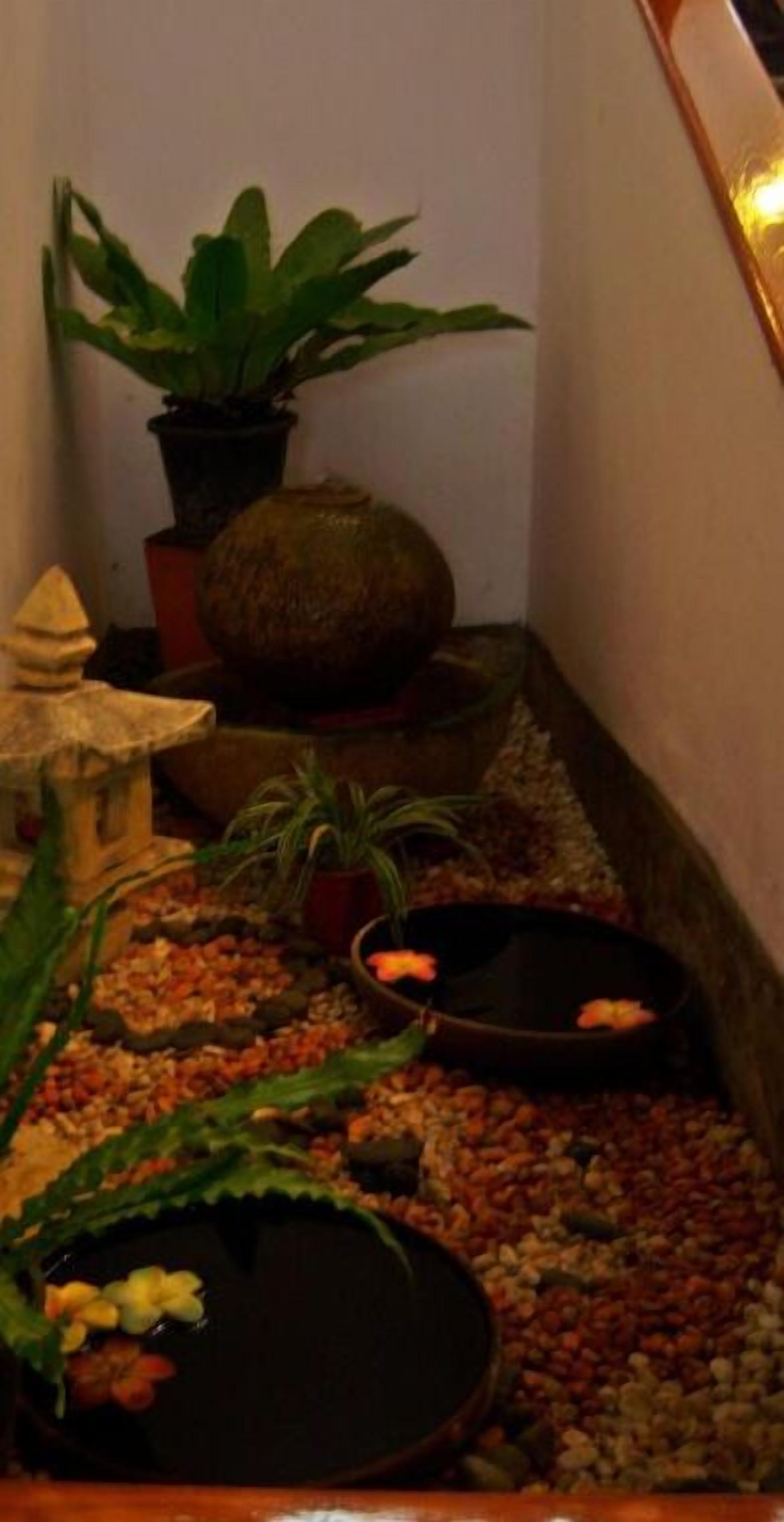 A narrow indoor space with a small fountain, potted plants, and a decorative stone structure.
