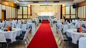 A banquet hall with round tables, white chairs, a red carpet, and a stage with floral decorations. - Tangerine Ville Hotel (Fang)