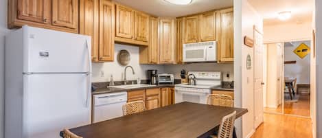 A kitchen with wooden cabinets, a white refrigerator, a microwave, and a stove. There is a dining table with chairs.