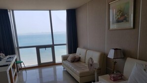 A hotel room with a large window offering a view of the sea, a sofa, a bed, and a desk with a chair. - Pohang Valentine Hotel (Pohang)