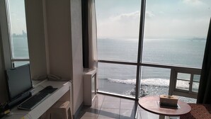 A room with a large window overlooking the sea, a desk with a computer, and a small round table with a box on it. - Pohang Valentine Hotel (Pohang)