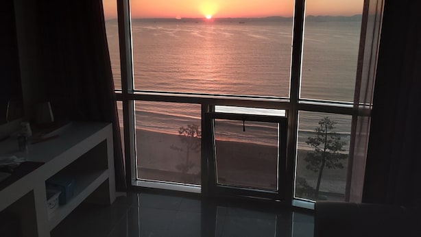 A room with a large window overlooking a sunset over the sea. - Pohang Valentine Hotel (Pohang)