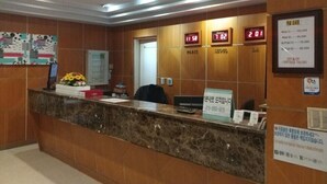 A reception desk with a marble top, a clock displaying 11:58, and a sign with a phone number. - Pohang Valentine Hotel (Pohang)