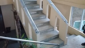 A staircase with metal railings and a handrail, leading to a landing with a view of the outside. - Rangala Hostel (Rangala)