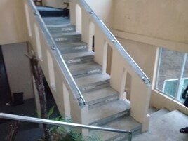 Una escalera con barandillas y pasamanos metálicos, que lleva a un rellano con vistas al exterior.