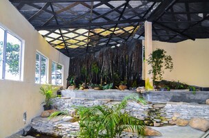 Un espacio al aire libre techado con escalones de piedra, plantas en macetas y una pequeña fuente.
