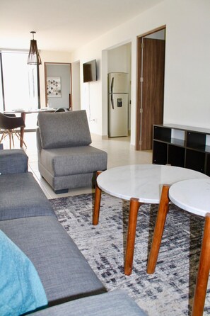 Un salon moderne avec un canapé gris, une table ronde et un téléviseur à écran plat fixé au mur.