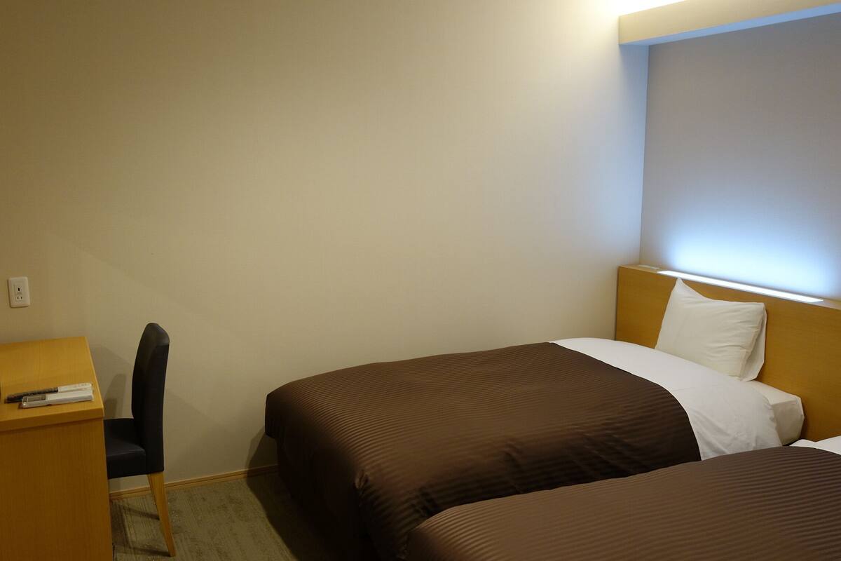 Quarto de hotel com duas camas, uma escrivaninha e uma cadeira.
