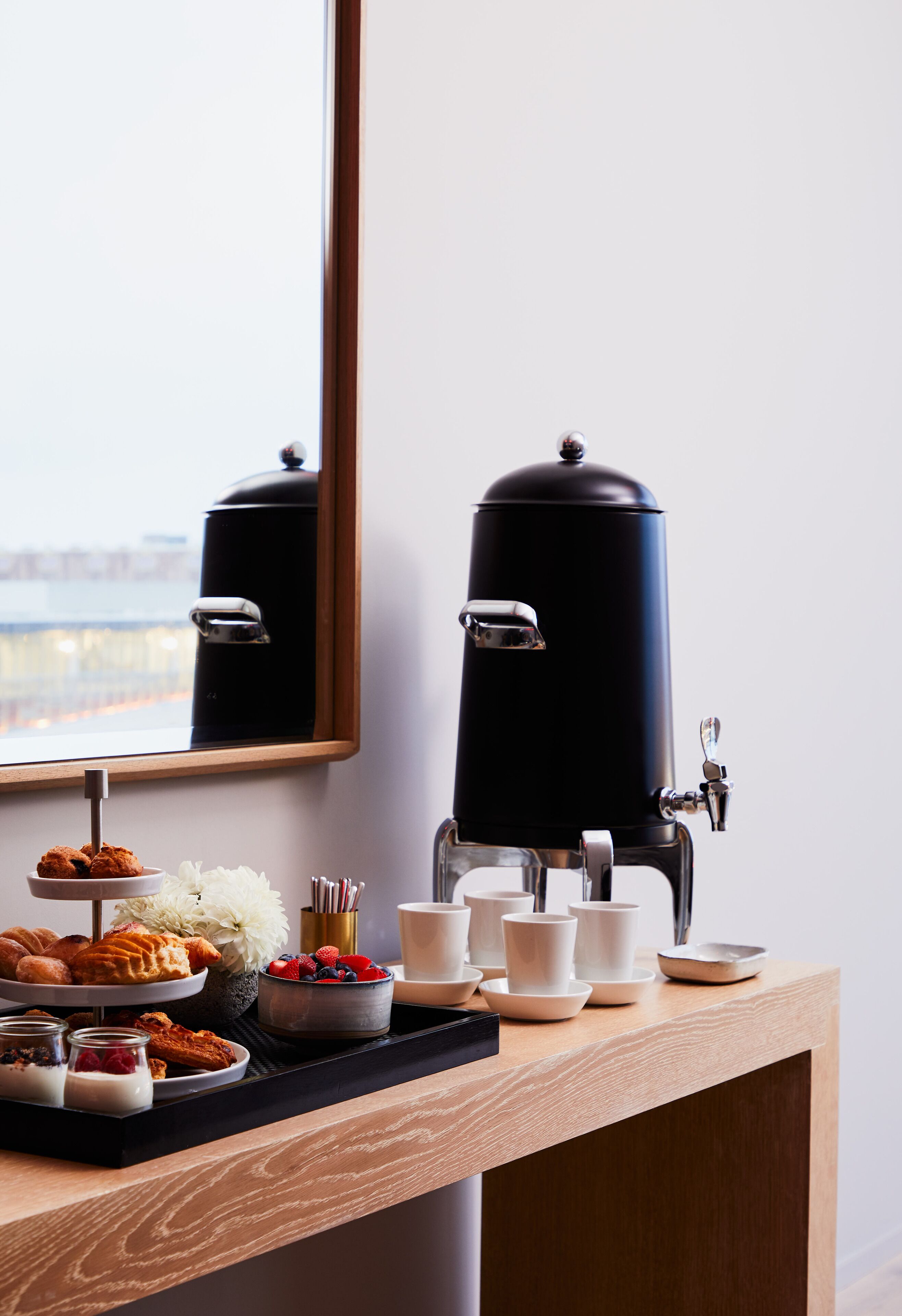 A breakfast buffet setup with a coffee machine, pastries, and a flower arrangement on a wooden table.