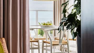 A room with a view of the sea, a table with chairs, a lamp, and a large plant.