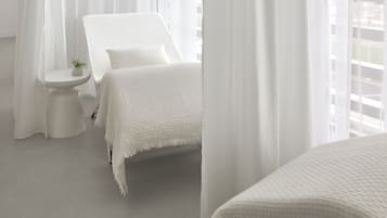 A room with a bed, a small table with a plant, and sheer white curtains.