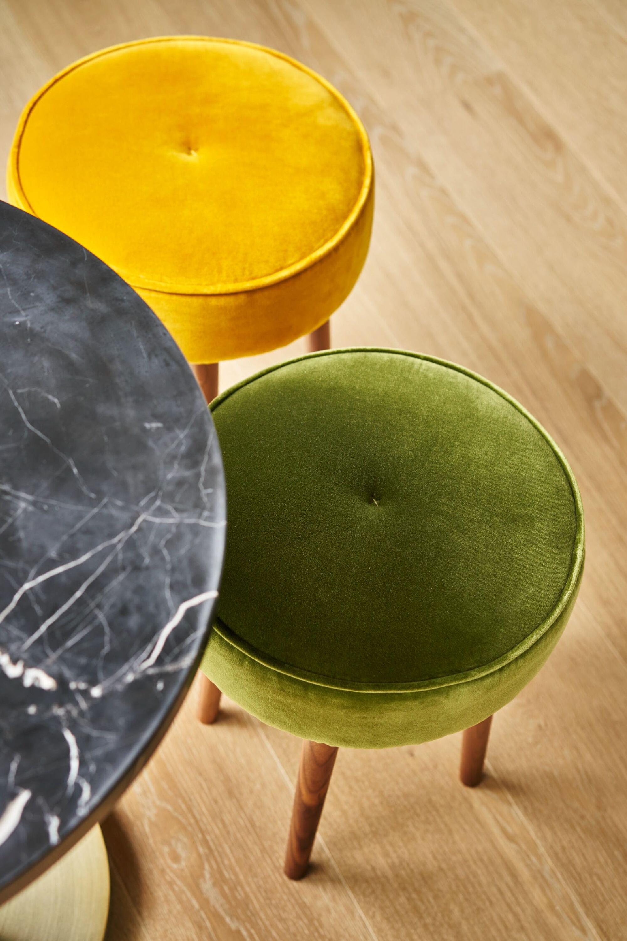 Three round ottomans in yellow, green, and black colors on wooden legs.