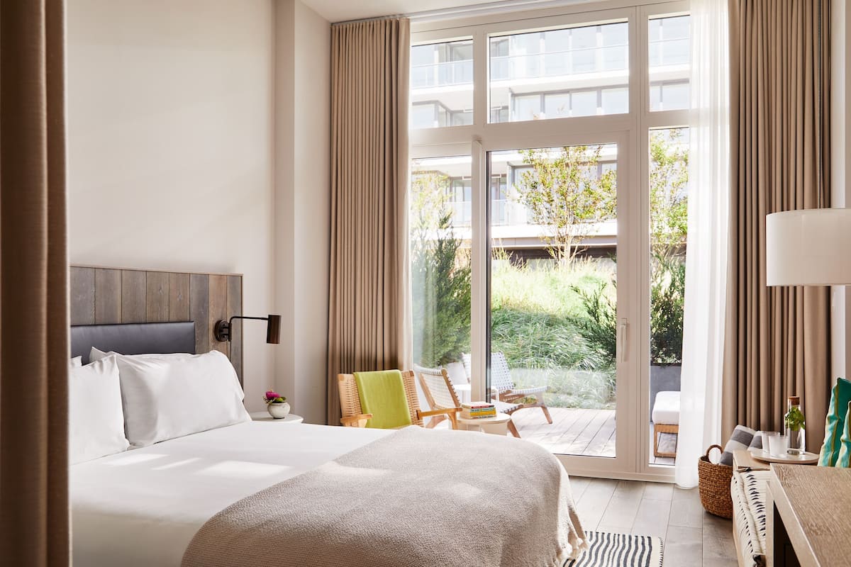 Ein Hotelzimmer mit Bett, Sessel, Tisch und Blick ins Freie.