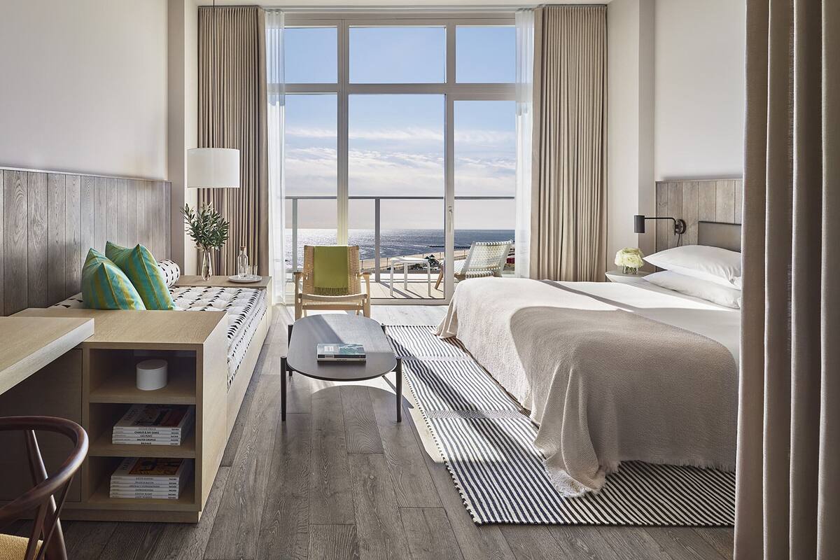 Ein Hotelzimmer mit Bett, Schreibtisch, Stuhl, einem kleinen Tisch und Blick aufs Meer.