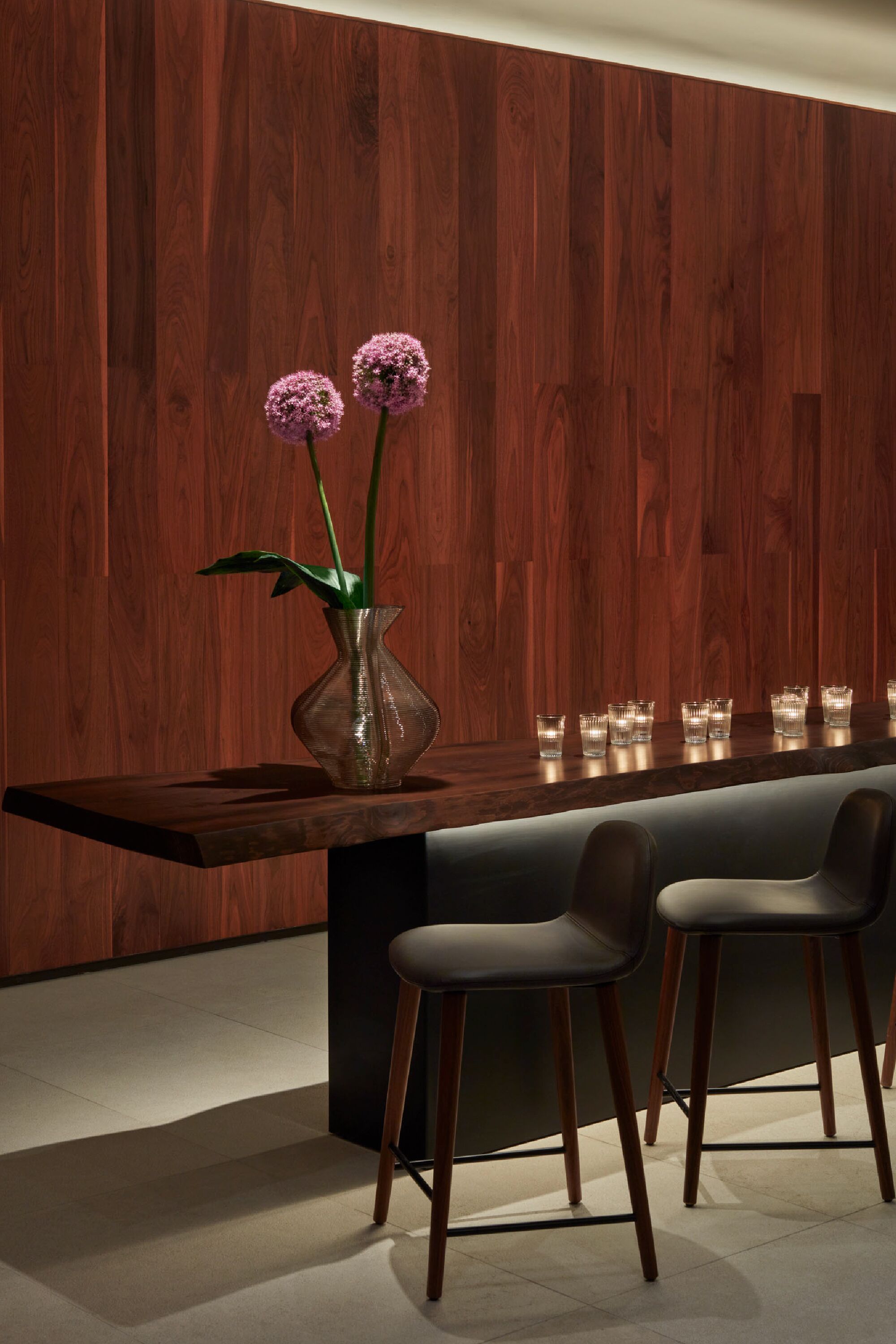 A modern bar area with a wooden wall, a vase with flowers, and bar stools.