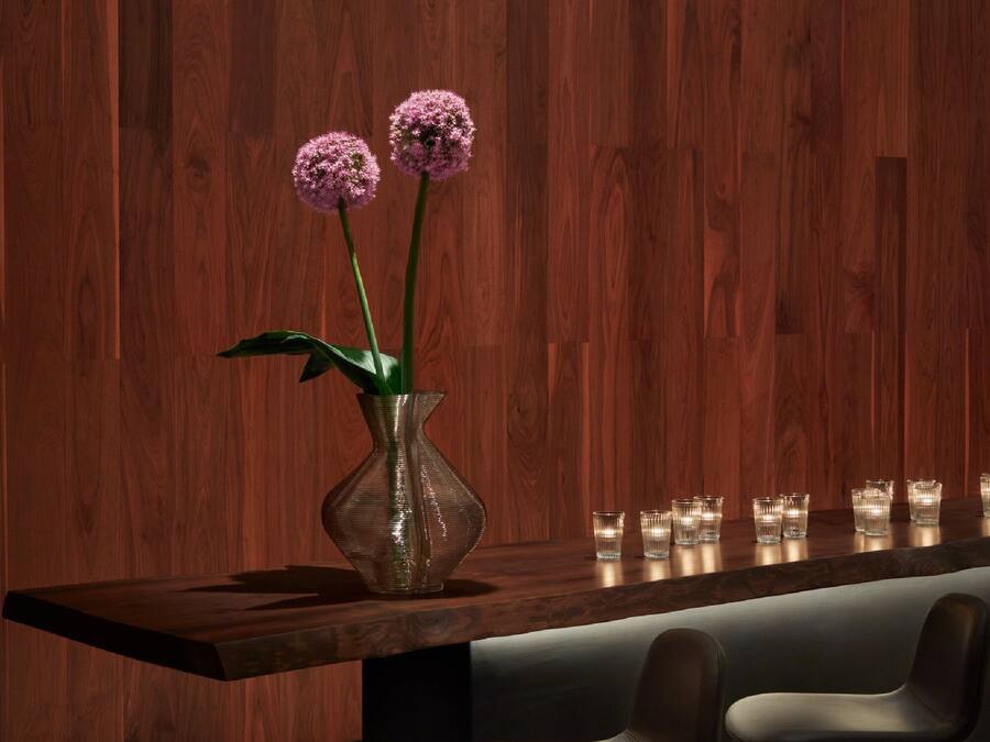 A modern bar area with a wooden wall, a vase with flowers, and bar stools.