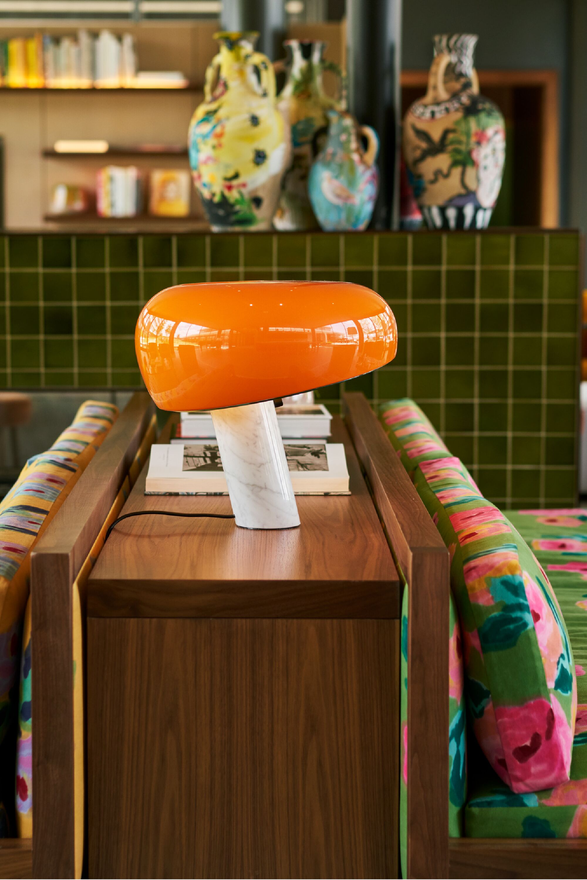 A wooden side table with a white marble base and an orange lamp.