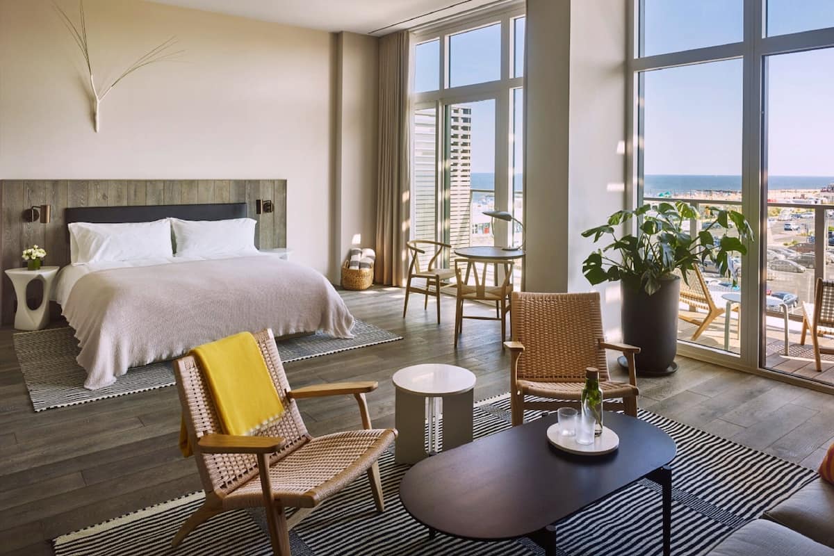 Ein modernes Hotelzimmer mit einem großen Bett, einem Balkon mit Blick auf die Stadt und einer Sitzecke mit Tisch und Stühlen.