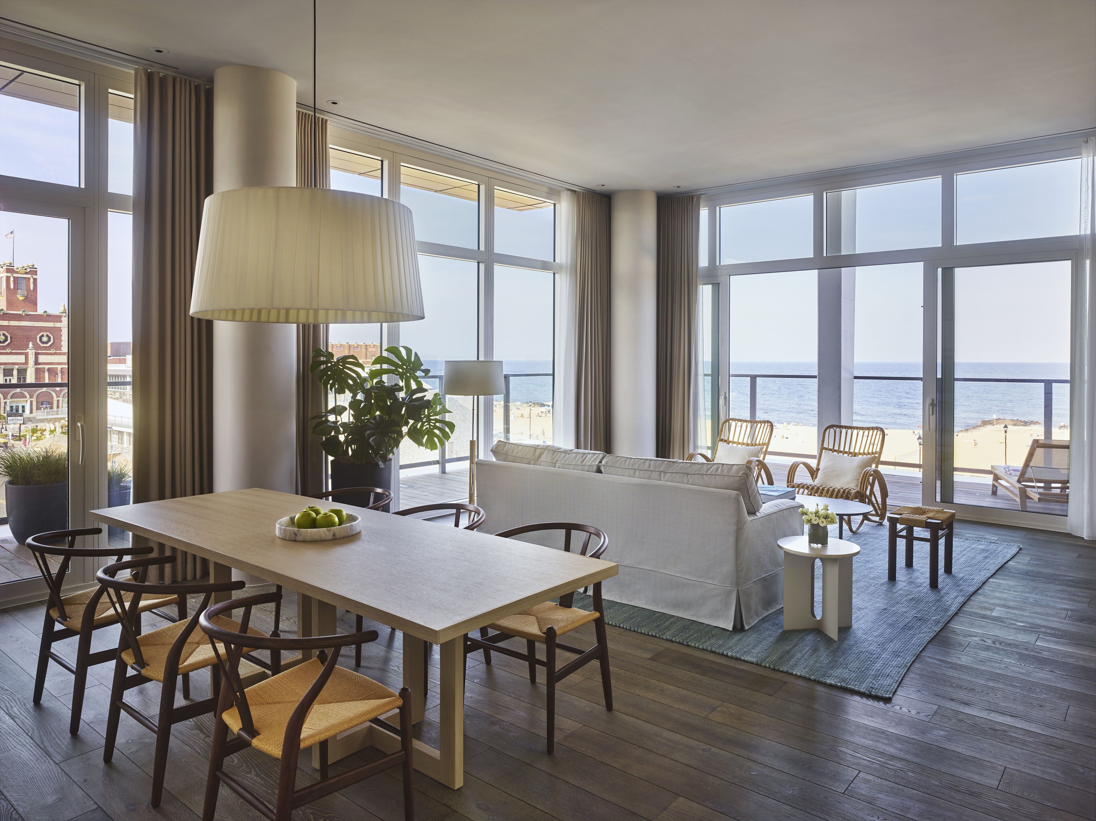 Una habitació àmplia amb un gran taula de dinar, cadires i un sofà. Té grans finestres amb vista a la platja i l'oceà.