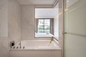 Un baño moderno con una bañera grande, una cabina de ducha de vidrio y vistas a un balcón con una cama.