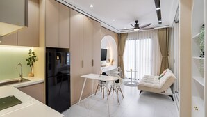 A modern kitchen with a black refrigerator, white dining table, and chairs. There is a sofa and a small round table in the living area.