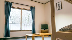 A room with a bed, a wooden table, a television, and a window with curtains. - Myoko House - Hostel (Myoko)