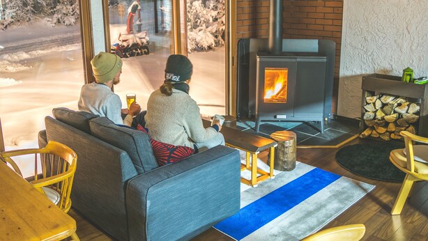 A cozy living room with a fireplace, a sofa, and a view of a snowy street outside. - Myoko House - Hostel (Myoko)
