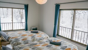 A bedroom with two beds, large windows with curtains, a ceiling light, and a small bedside table. - Myoko House - Hostel (Myoko)
