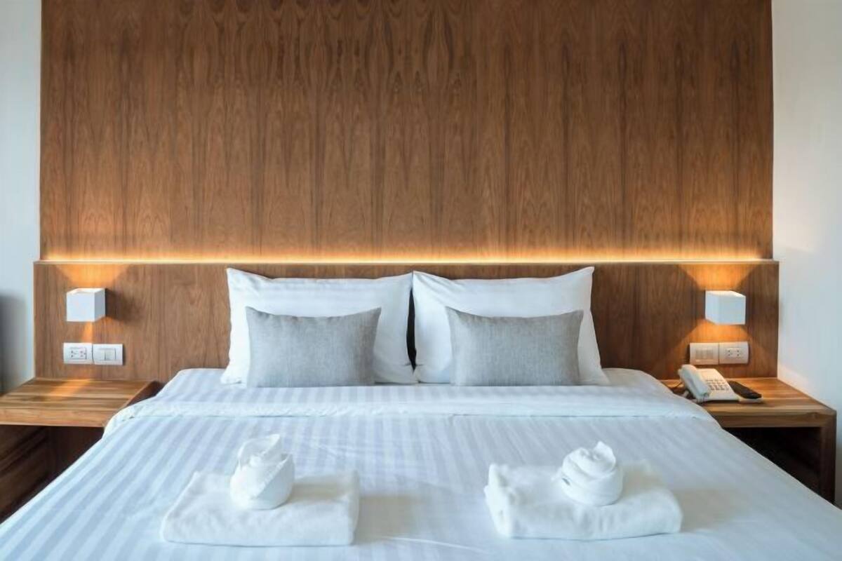 A hotel room with a wooden headboard, two bedside tables with lamps, a bed with white linens, and two towels on the bed.