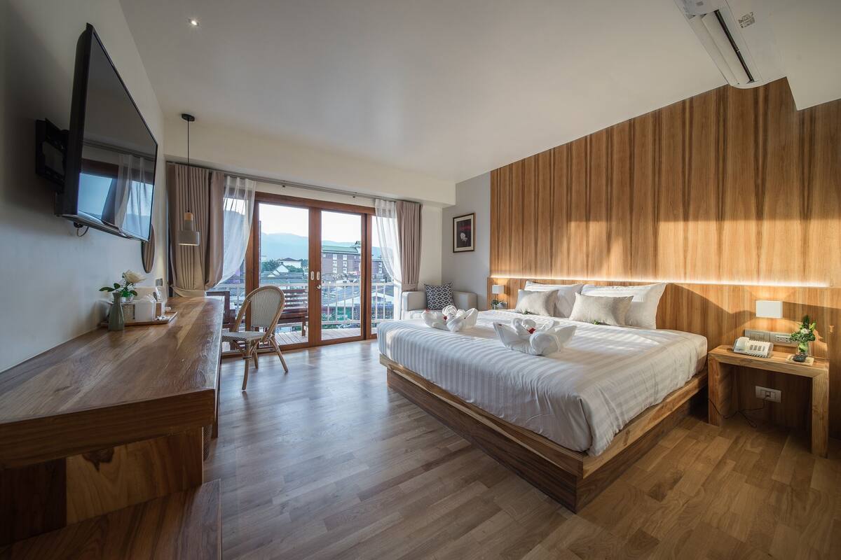 A hotel room with a large bed, wooden desk, and a TV mounted on the wall.