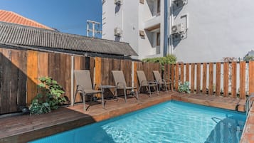 A swimming pool with lounge chairs, a wooden fence, and a building with air conditioning units.