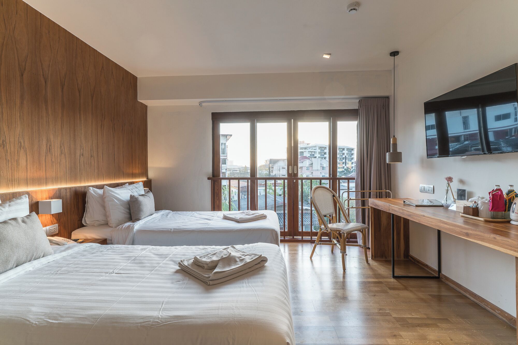 Habitación de hotel con dos camas, un escritorio, una silla, un televisor y un balcón con vistas a la ciudad.
