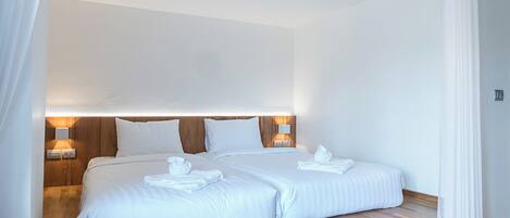 Cama doble con sábanas blancas, dos lámparas de noche, cabecera de madera y cortina blanca.
