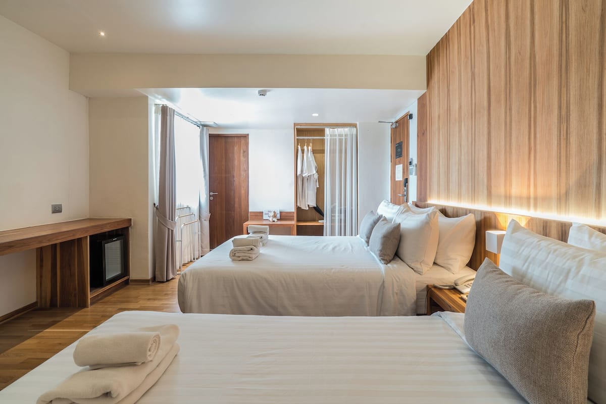 A hotel room with two beds, a wooden wardrobe, a desk, and a mirror.