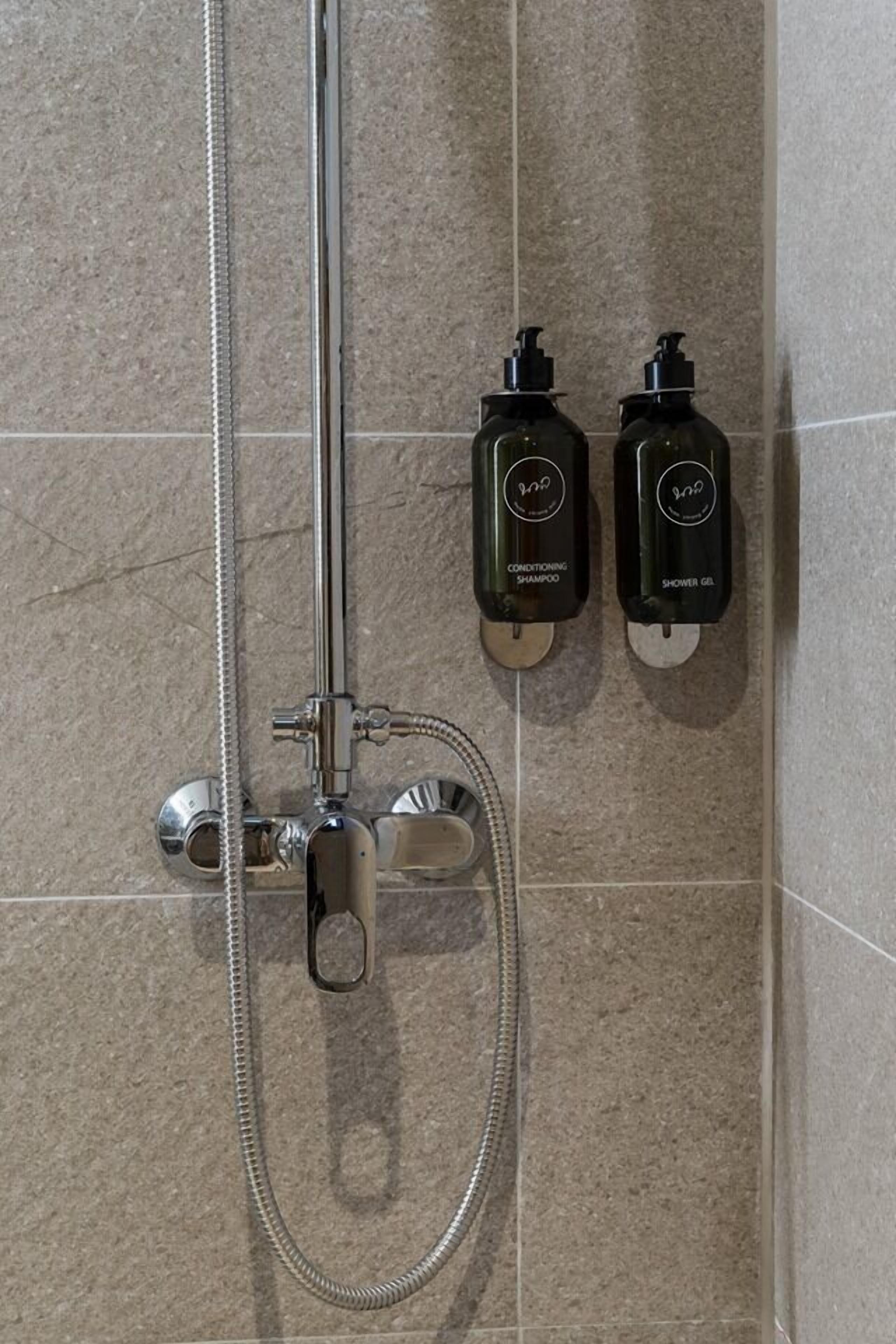 Ein Duschbereich mit Handbrause sowie zwei Flaschen Shampoo und Duschgel.
