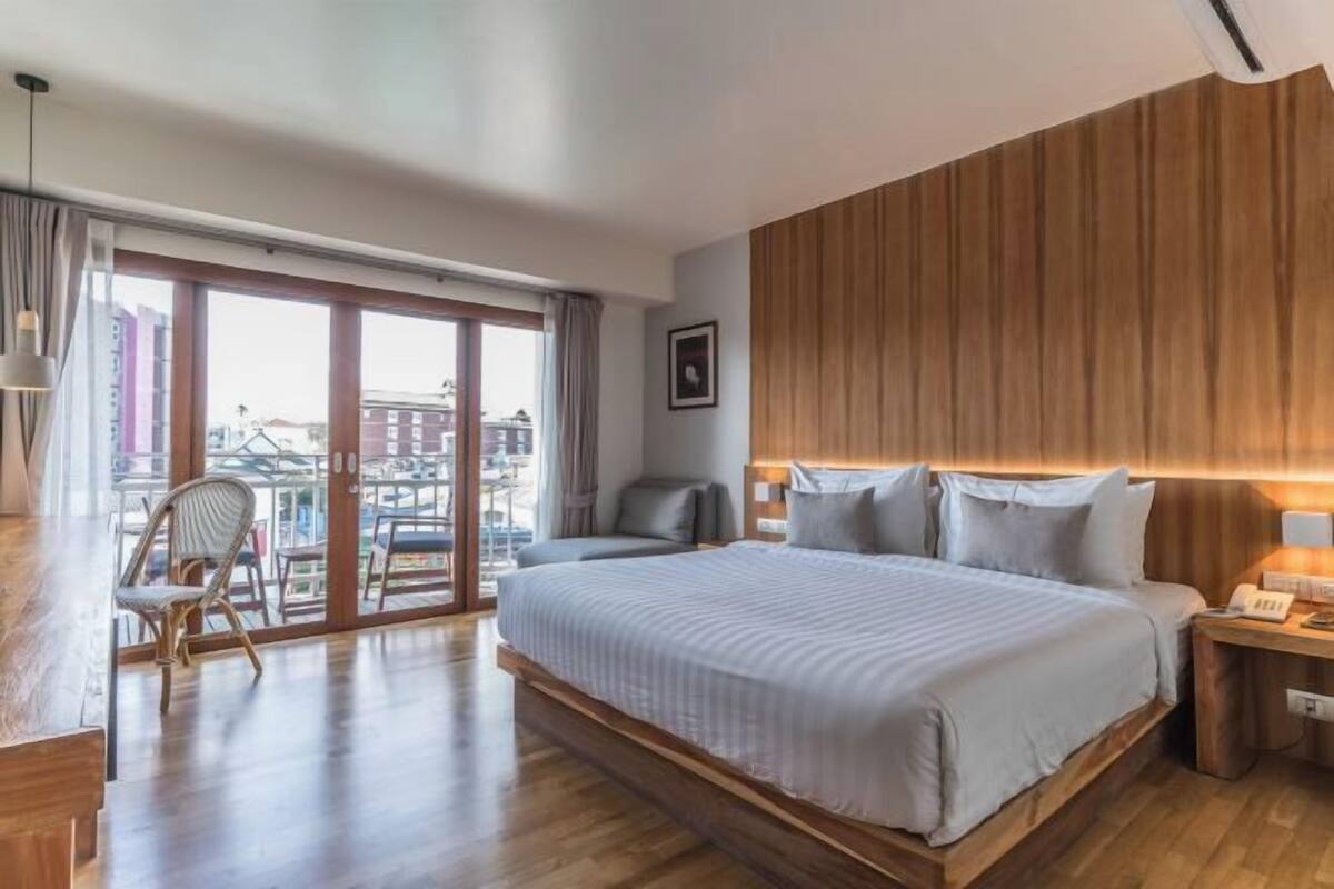 A hotel room with a large bed, a chair, a desk, and a view of the city through a large window.