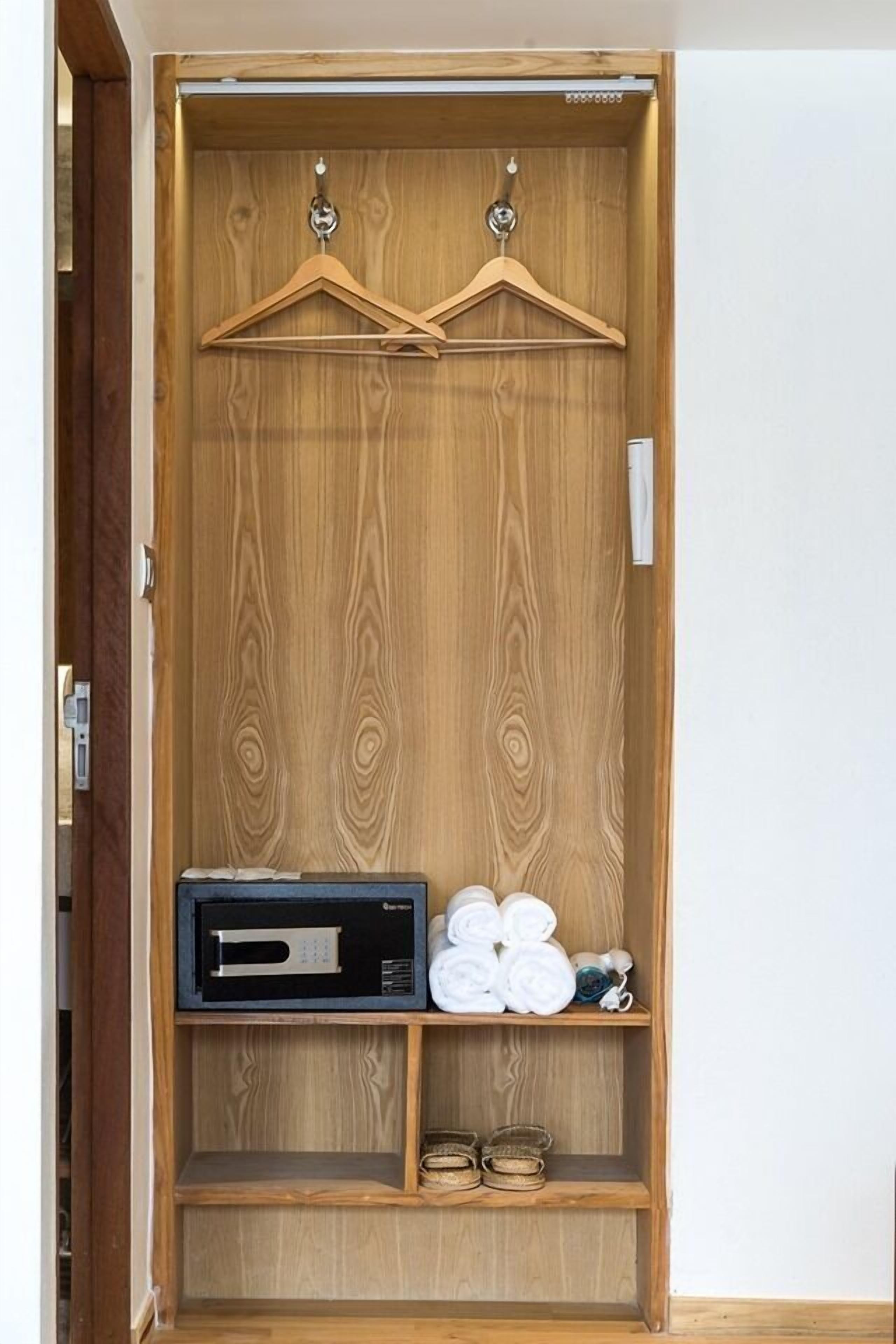 A wooden wardrobe with two hanging spaces, a microwave, and a shelf with rolled towels and shoes.