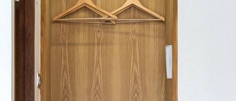 A wooden wardrobe with two hanging spaces, a microwave, and a shelf with rolled towels and shoes.