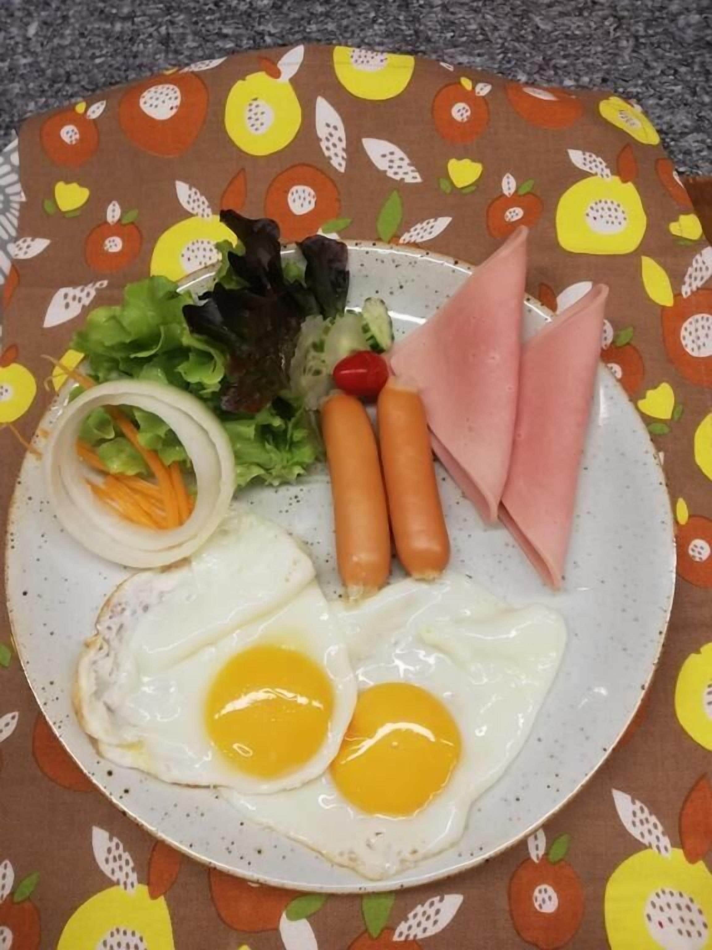 Ein Teller mit Eiern, Schinken, Karotten und Salat auf einer Tischdecke mit Fruchtmuster.