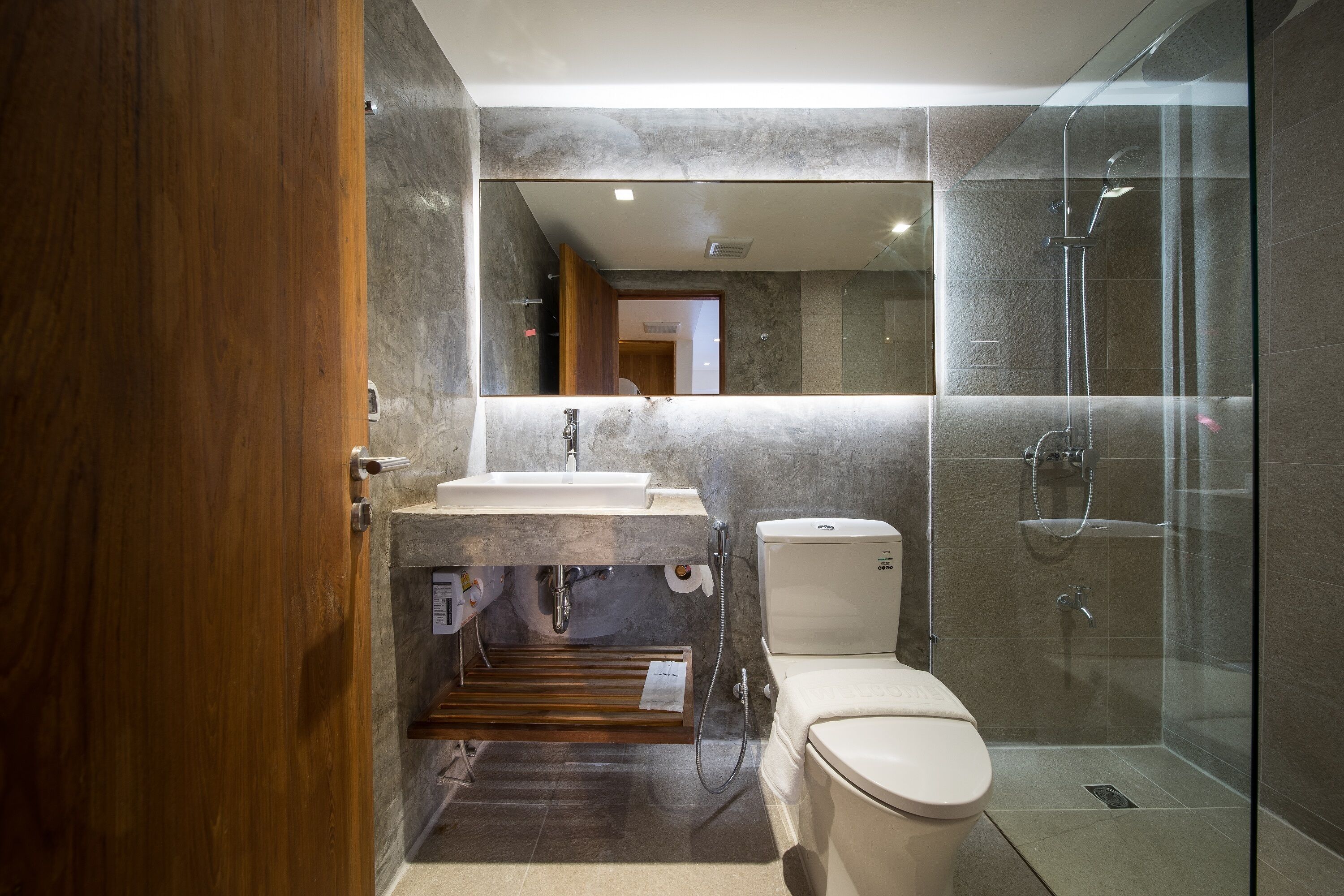 Un bany modern amb una porta de fusta, un lavabo, un vàter i una dutxa amb envàs de vidre.