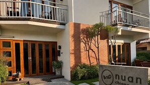 Un edificio con un letrero que dice 'nuan chiang mai', que presenta una puerta de madera, un balcón y un pequeño jardín.