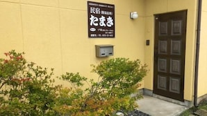 A building facade with a sign in Japanese, a door, and some greenery. - Tamaki (Fujiyoshida)